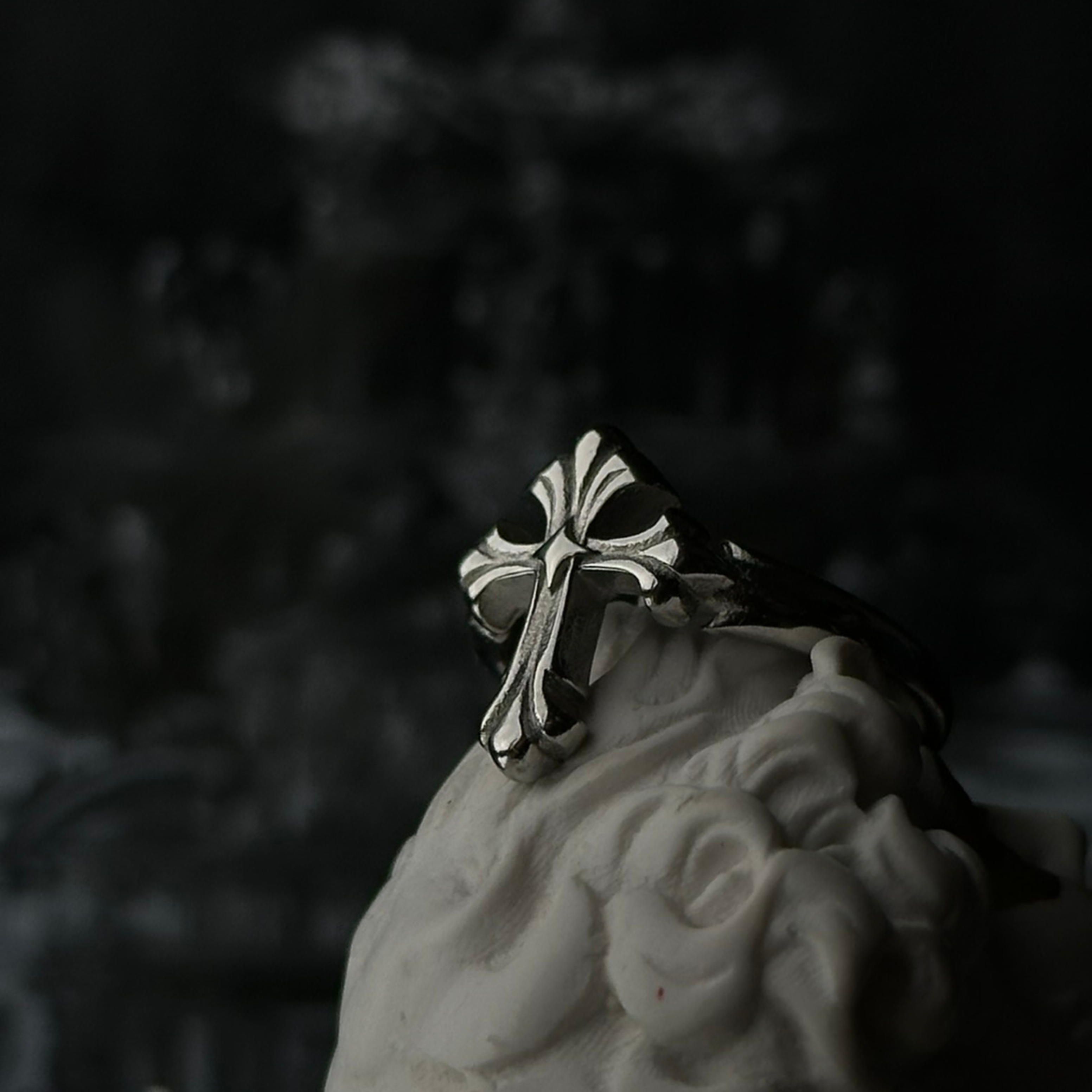 Anillo de acero inoxidable 'Follow Ring Lil Cross' con diseño de cruz en relieve, de la marca Follow God, exhibido sobre una figura decorativa blanca