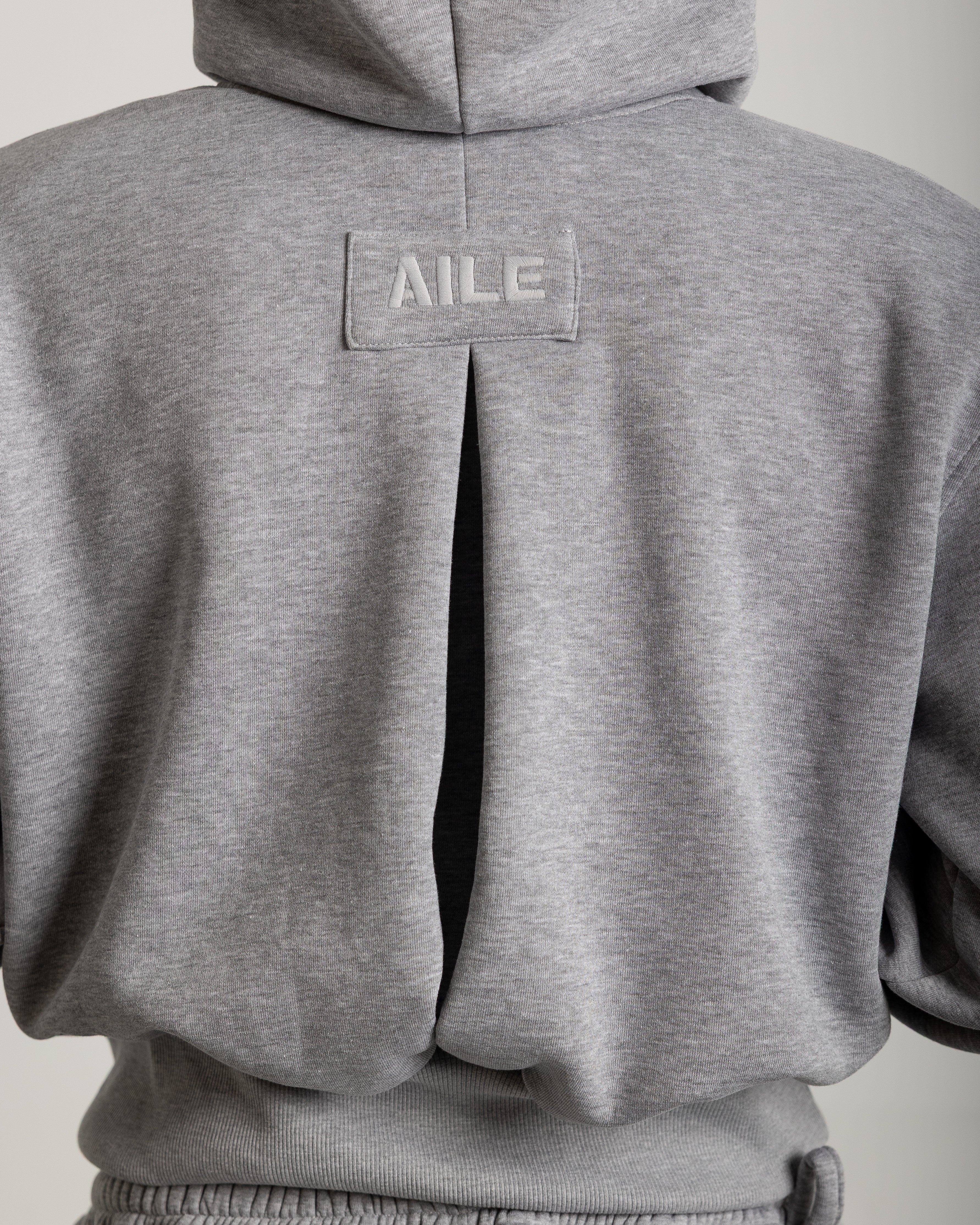 Grey 100% cotton sweatshirt with a kangaroo pocket. Double hood with a drawstring on the outer hood. Pleat at the back with grey embroidery at the top. Shoulder pads on the inside to give the garment structure.